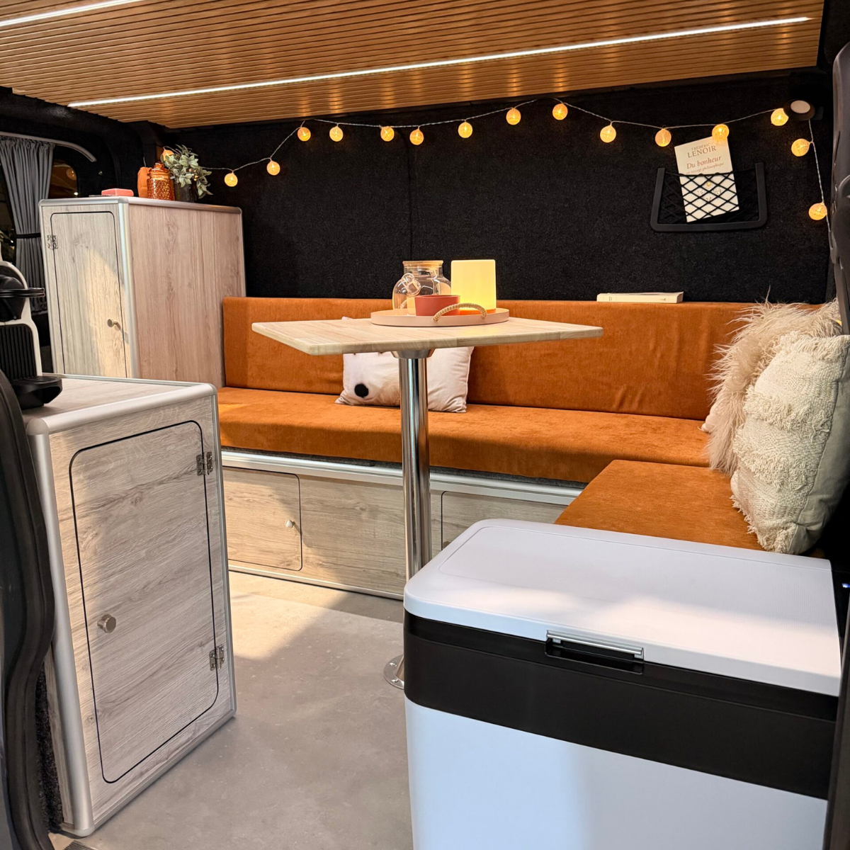 Ambiance cosy dans un van aménagé Sunset Van, banquette orange, table pivotante et glacière