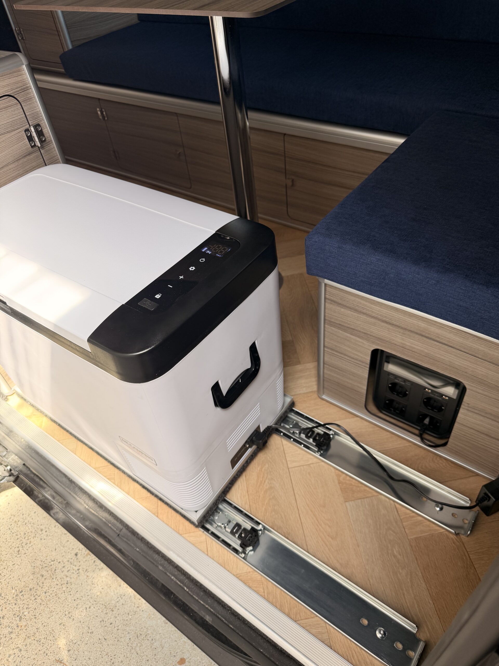 Réfrigérateur à compression encastré sur une banquette en bois dans un van aménagé par Sunset Van