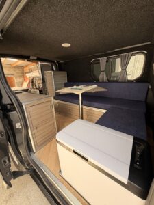 Aménagement intérieur en bois d'un van Sunset Van, avec banquette bleue et table amovible